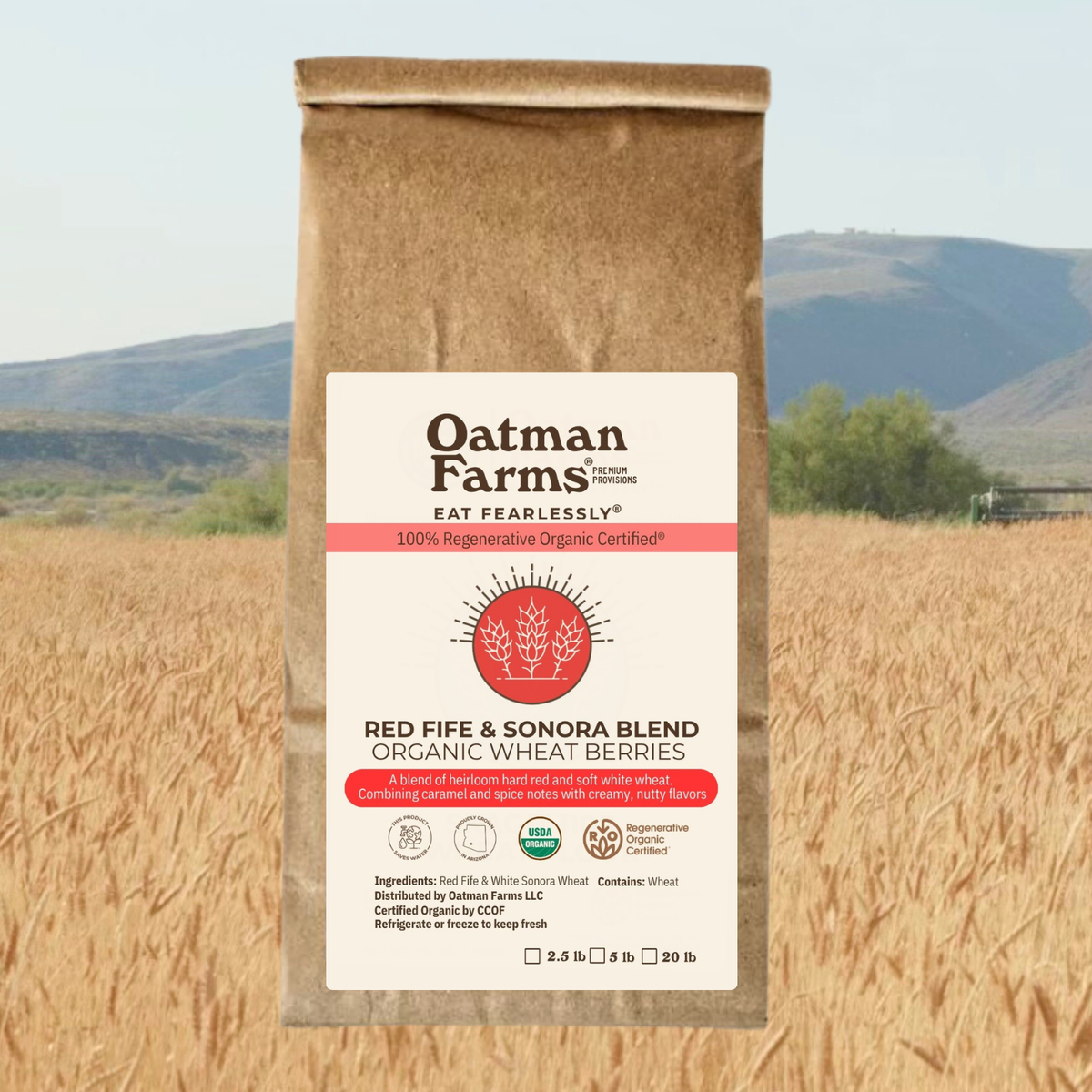 composite image of a brown bag labeled with Oatman Farms organic wheat berries imposed over a wheat field with mountains in the background.