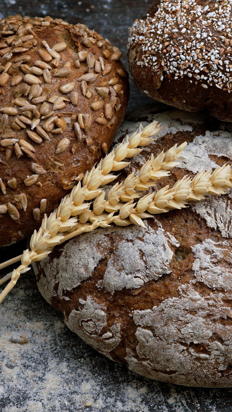 photo of the corners of three boulles of seeded bread with a wheat stalk in the center